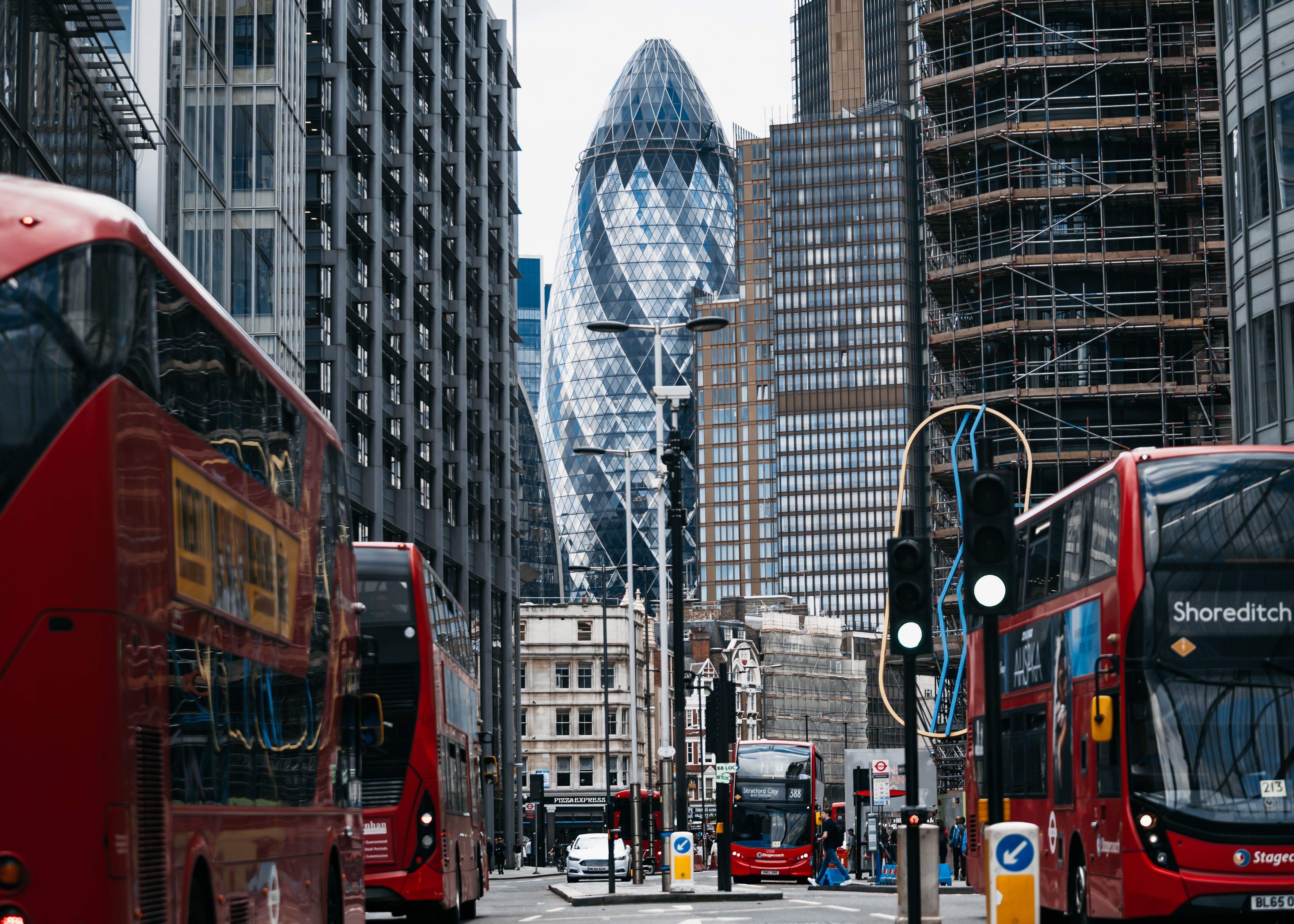 A bustling London street featuring red double-decker buses and the 30 St Mary Axe skyscraper.