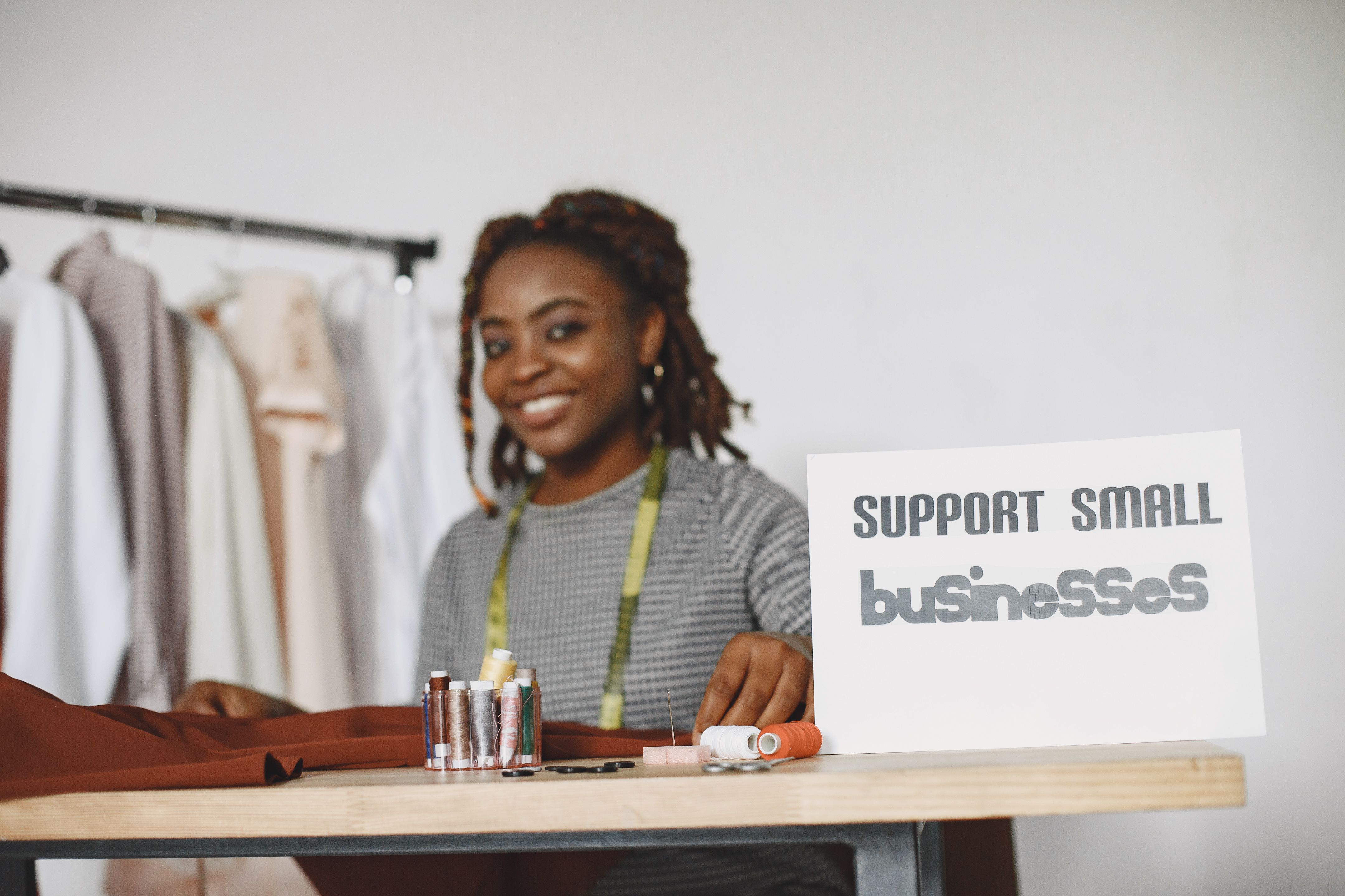 African American seamstress smiling at work with a 'Support Small Businesses' sign.