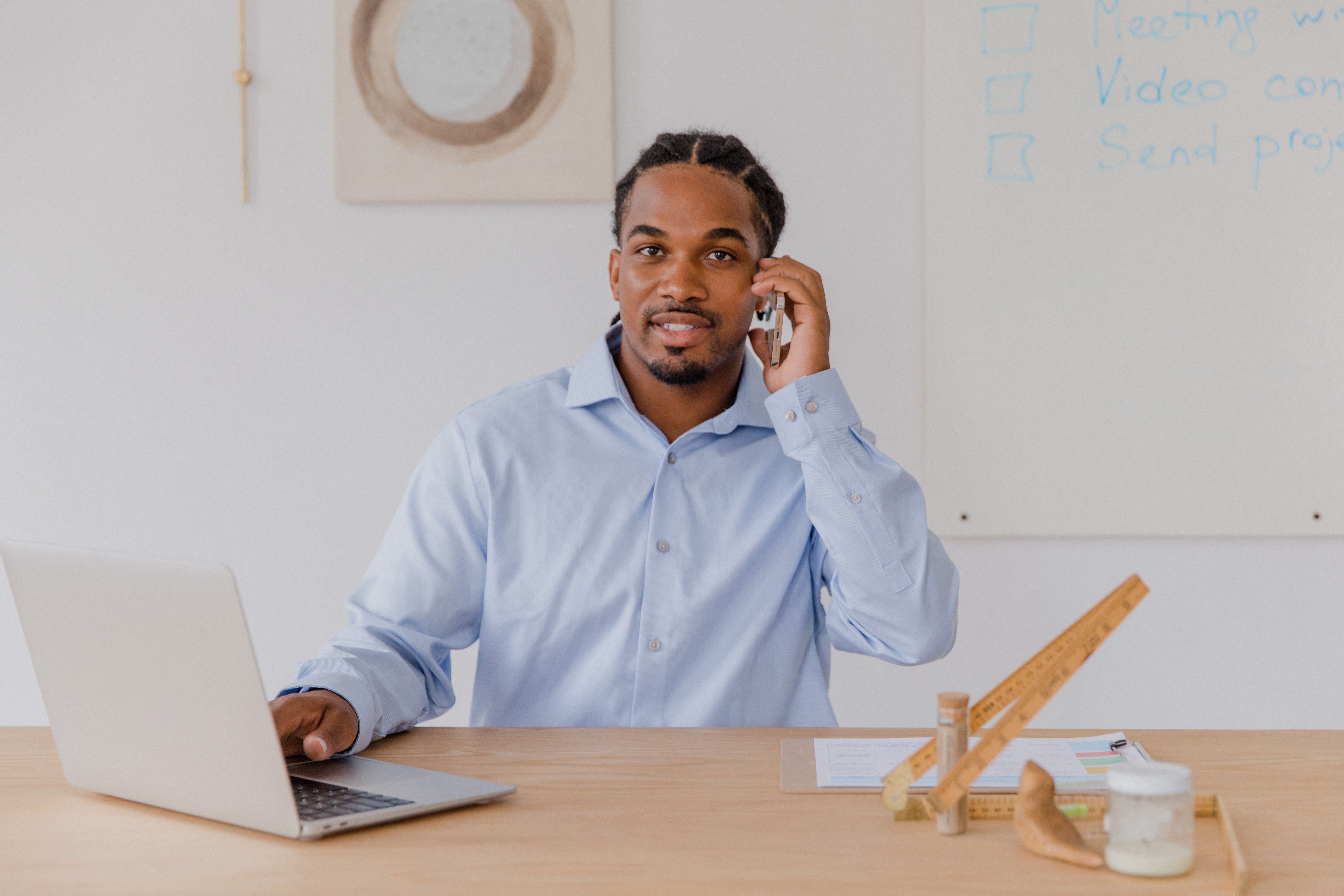 Young man at office desk on smartphone, using laptop, smiling. Professional work environment.