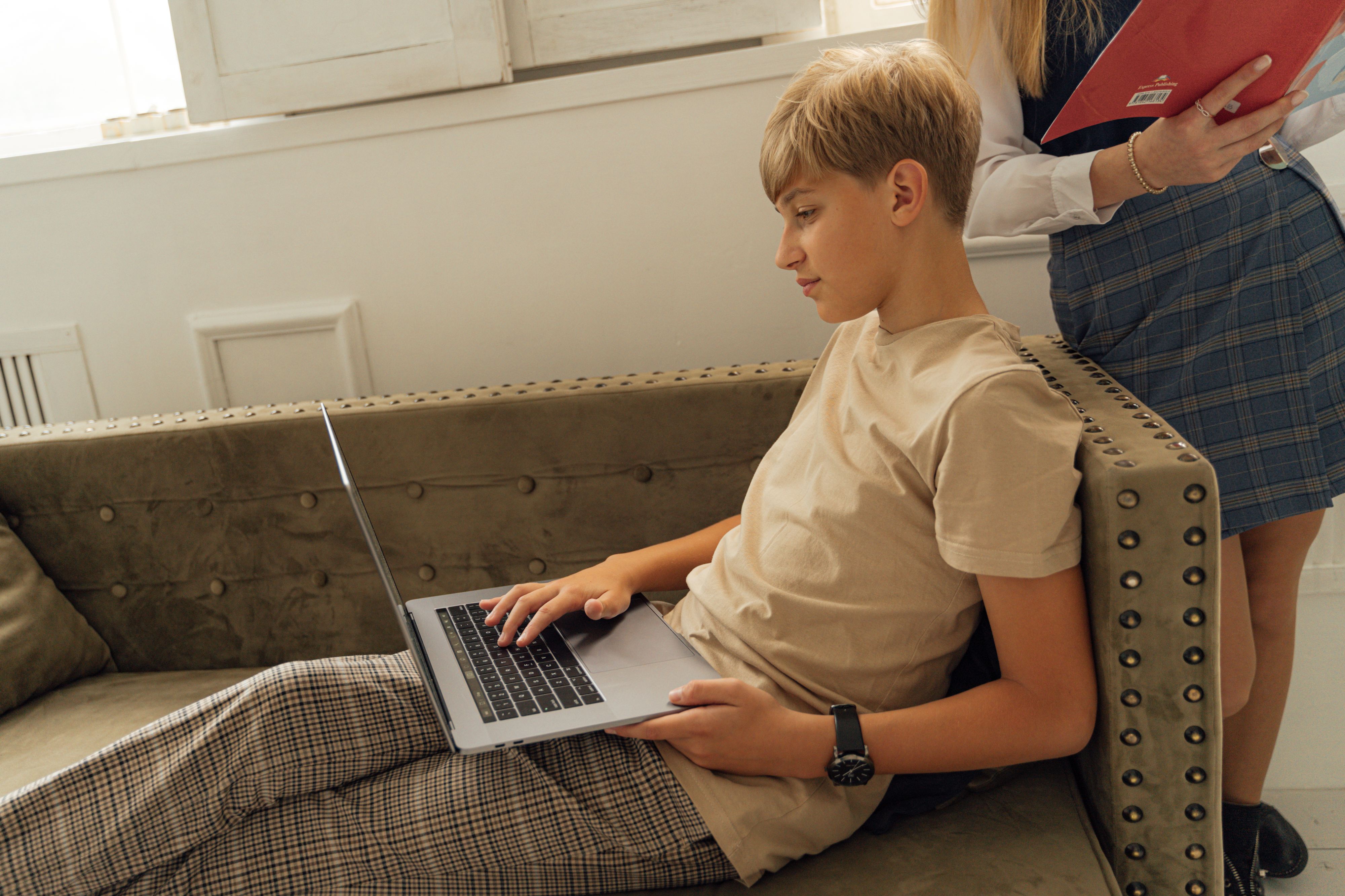 A teenager relaxing on a couch with a laptop, engaging in online learning indoors.