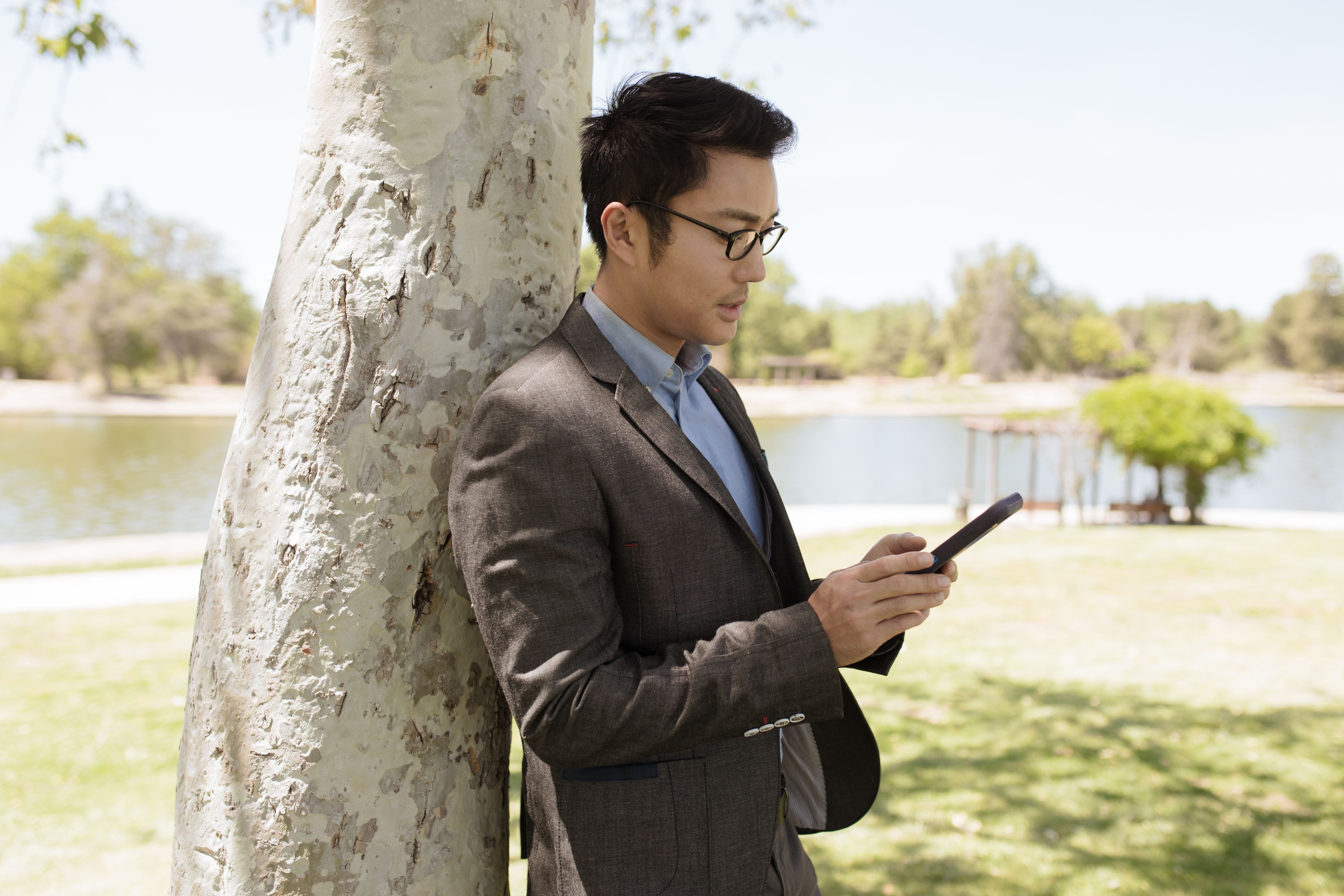 Stylish man in business attire using smartphone by a lakeside on a sunny day.