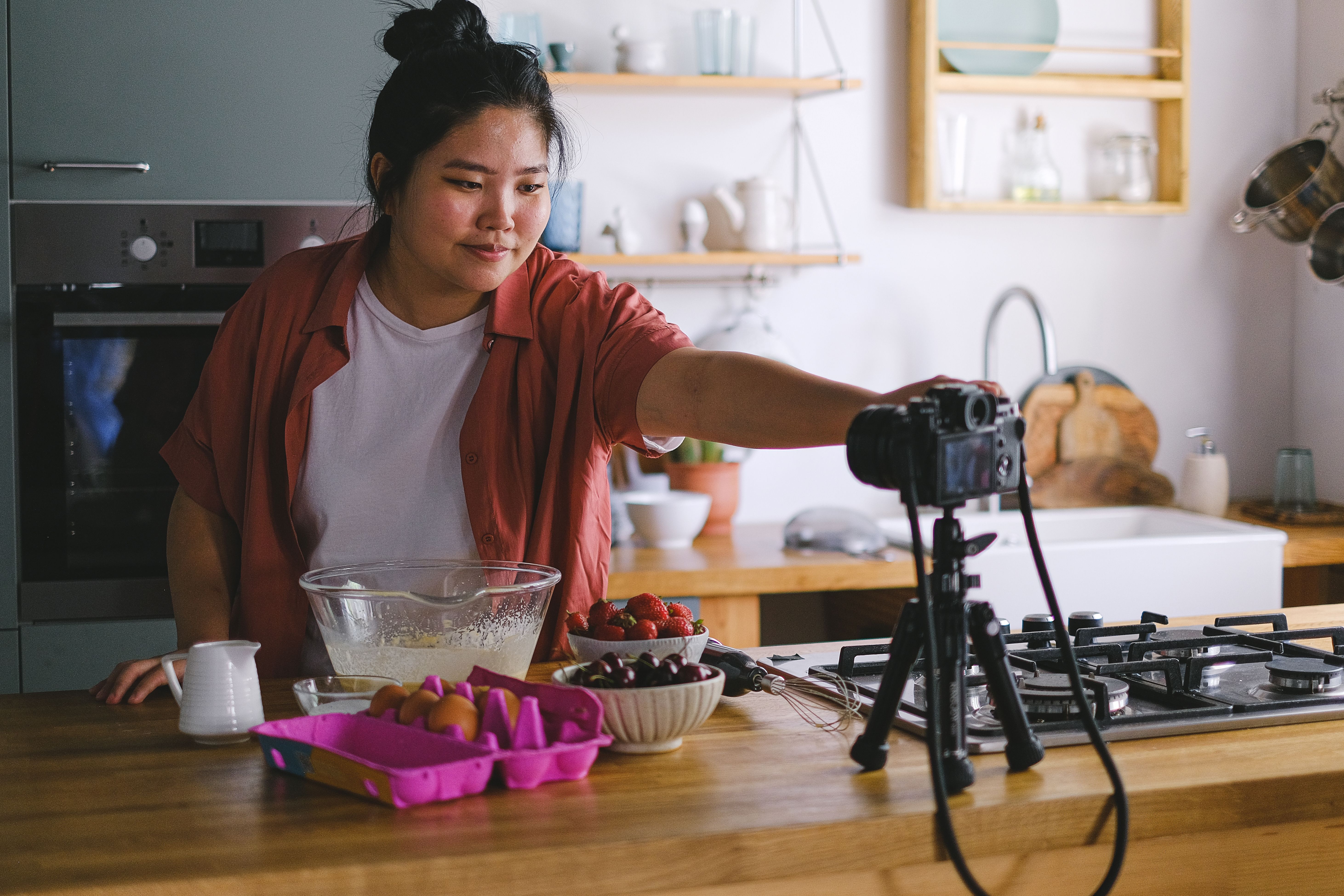 A woman films a cooking vlog in a cozy and modern kitchen with fresh ingredients.