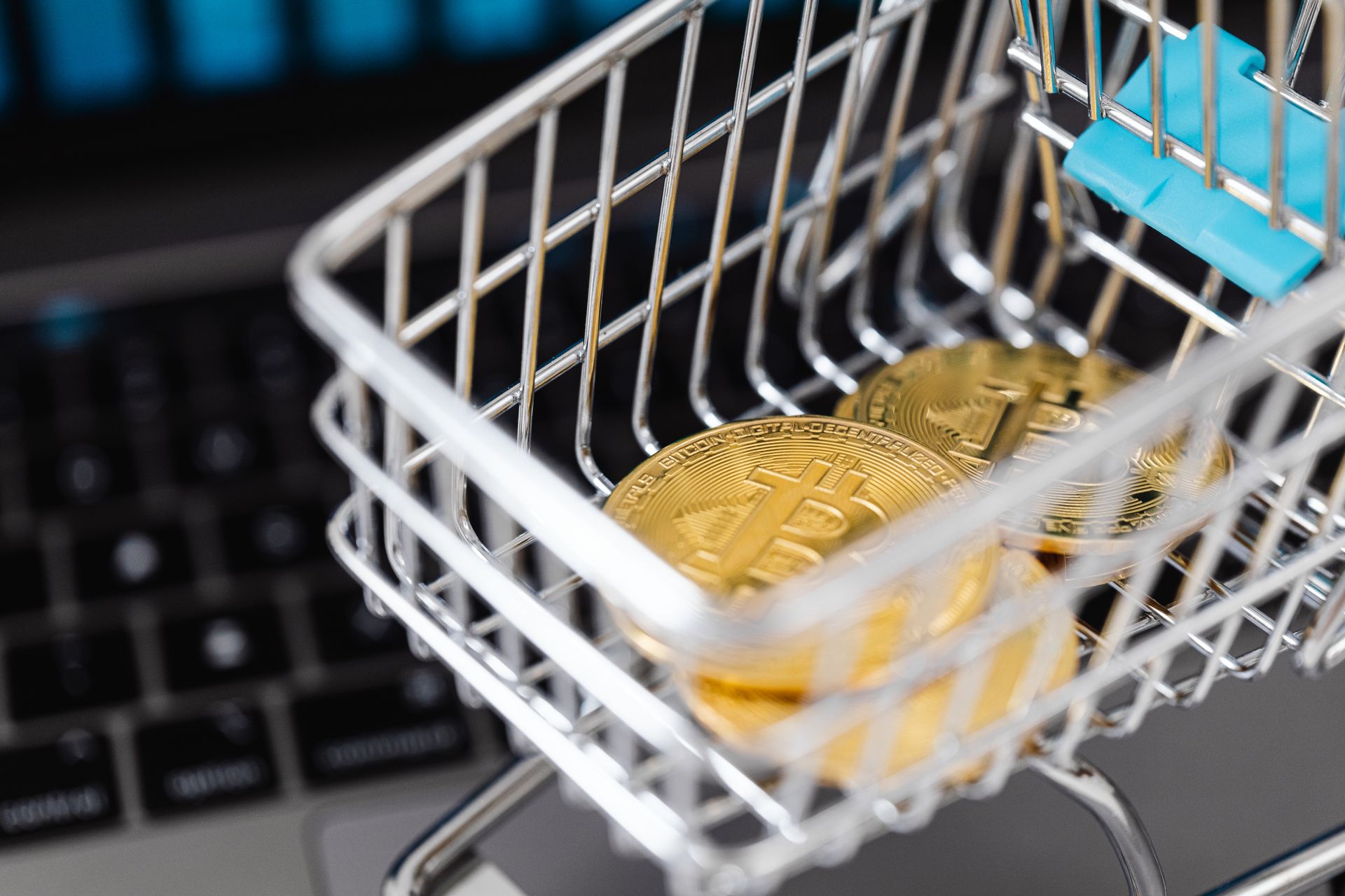 Miniature shopping cart holding physical gold bitcoins on top of a laptop keyboard representing a crypto payment gateway
