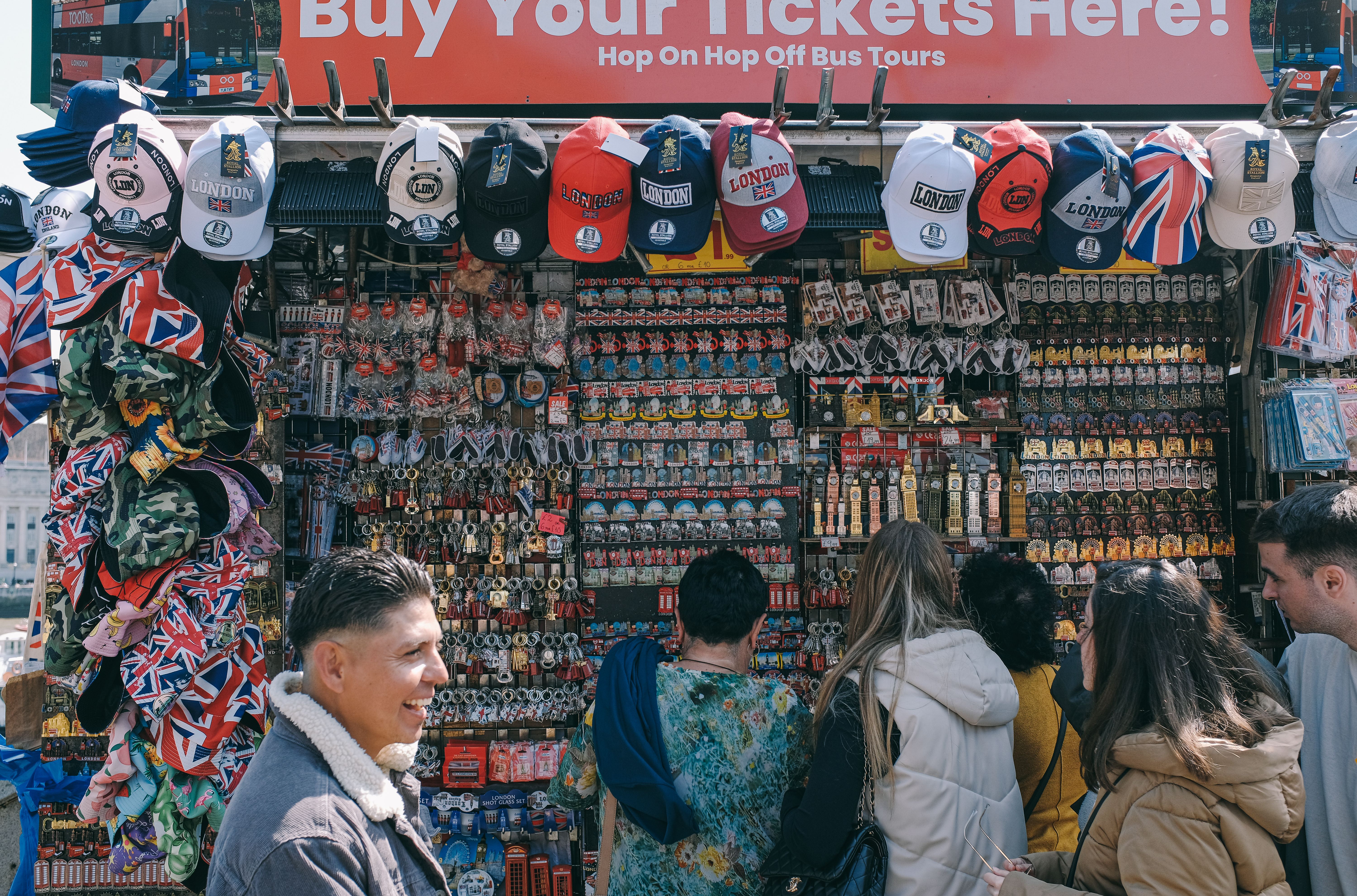 Colorful souvenir stall in London with tourists shopping for hats and memorabilia.